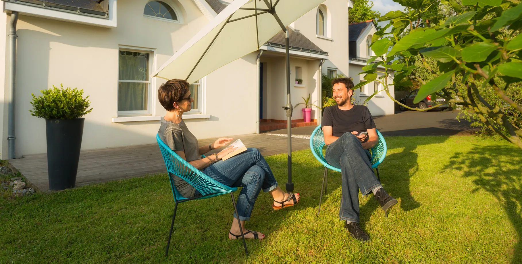 ombrellone inclinato con sistema Gard&Rock al centro di una terrazza in ghiaia, coppia che prende un aperitivo all’ombra