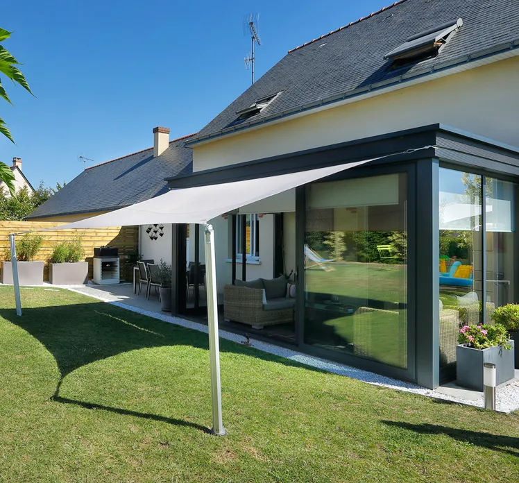 vela ombreggiante rettangolare tesa tra due pali telescopici davanti a una veranda